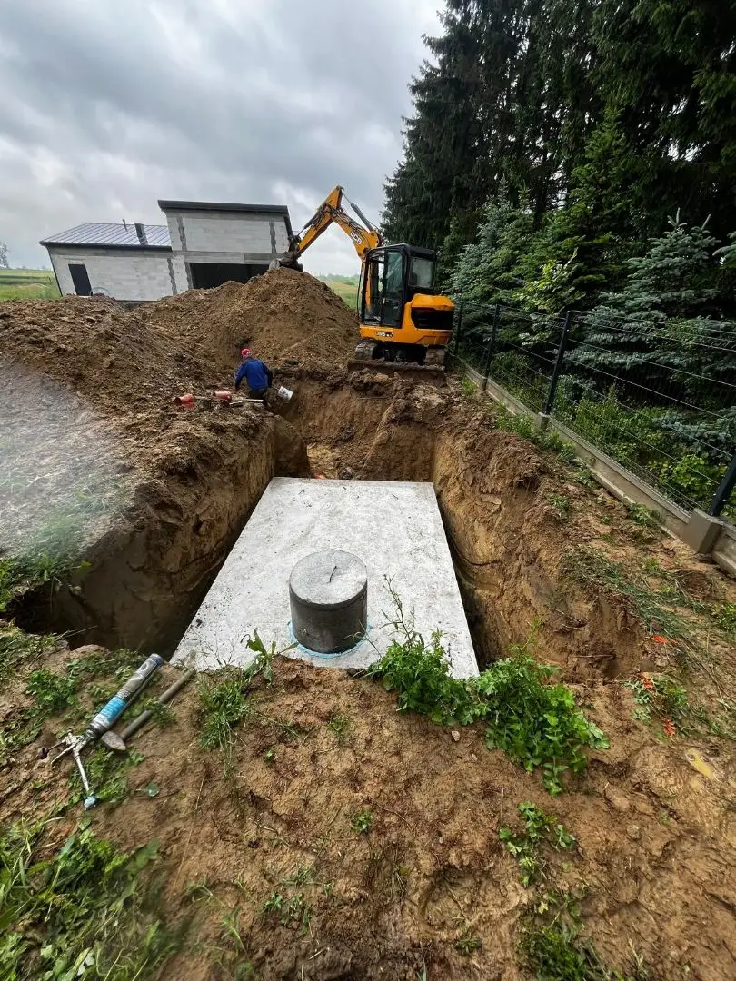 Szambo betonowe w wykopie - koparka JCB przy nowym domu