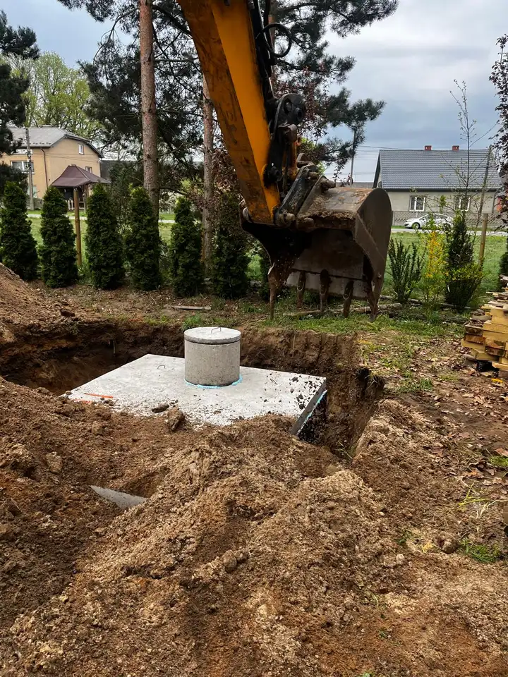 Montaż szamba betonowego przy tujach - koparka w pracy